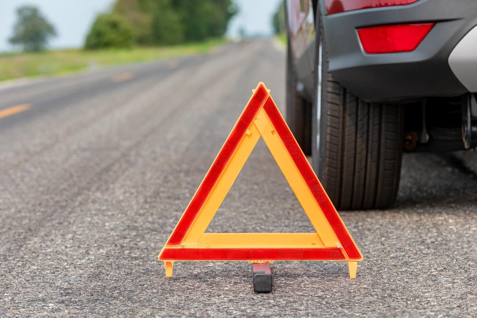 Red hazard triangle on asphalt road next to a stopped red vehicle, signaling a breakdown.