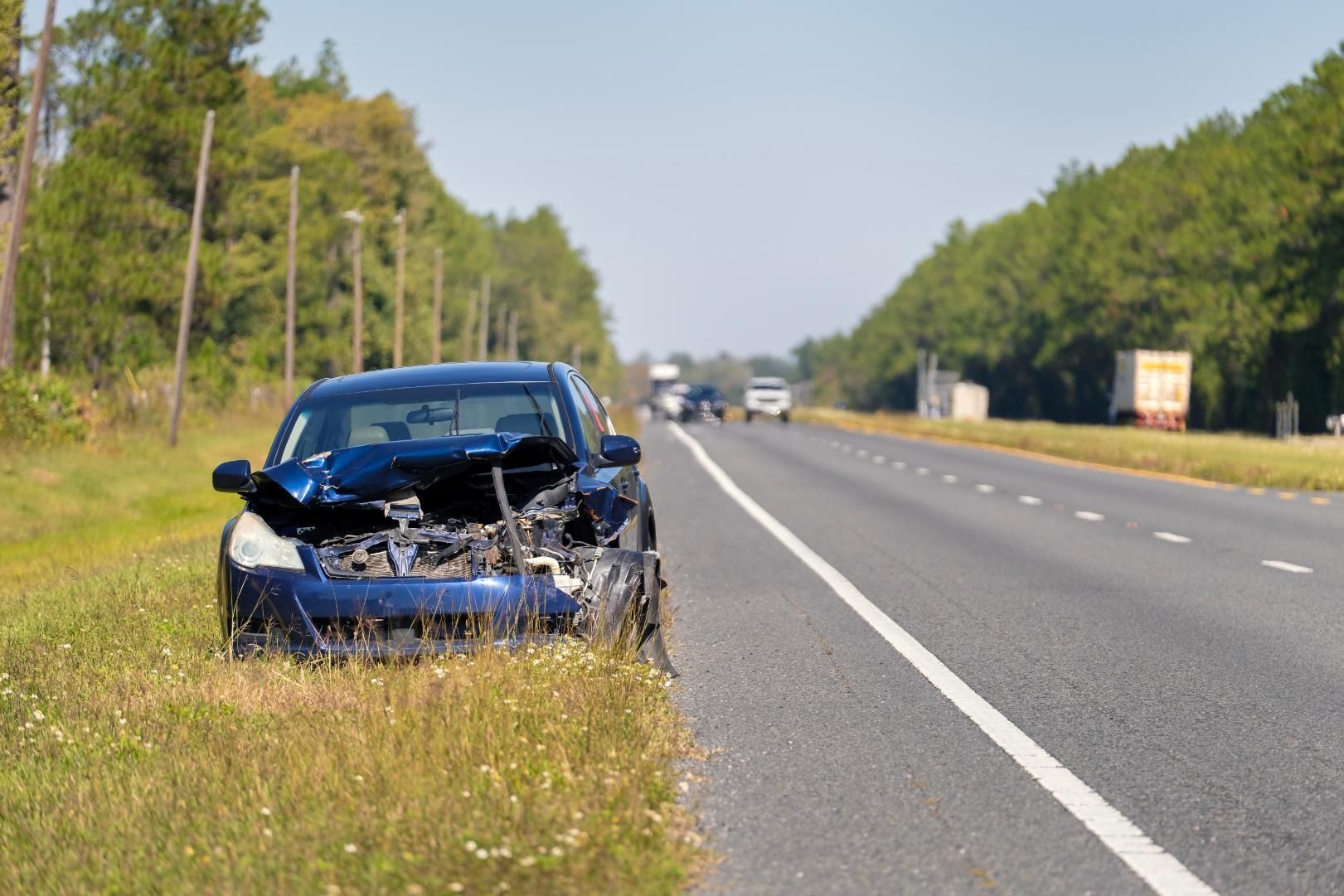 Damaged blue car off the side of a highway.