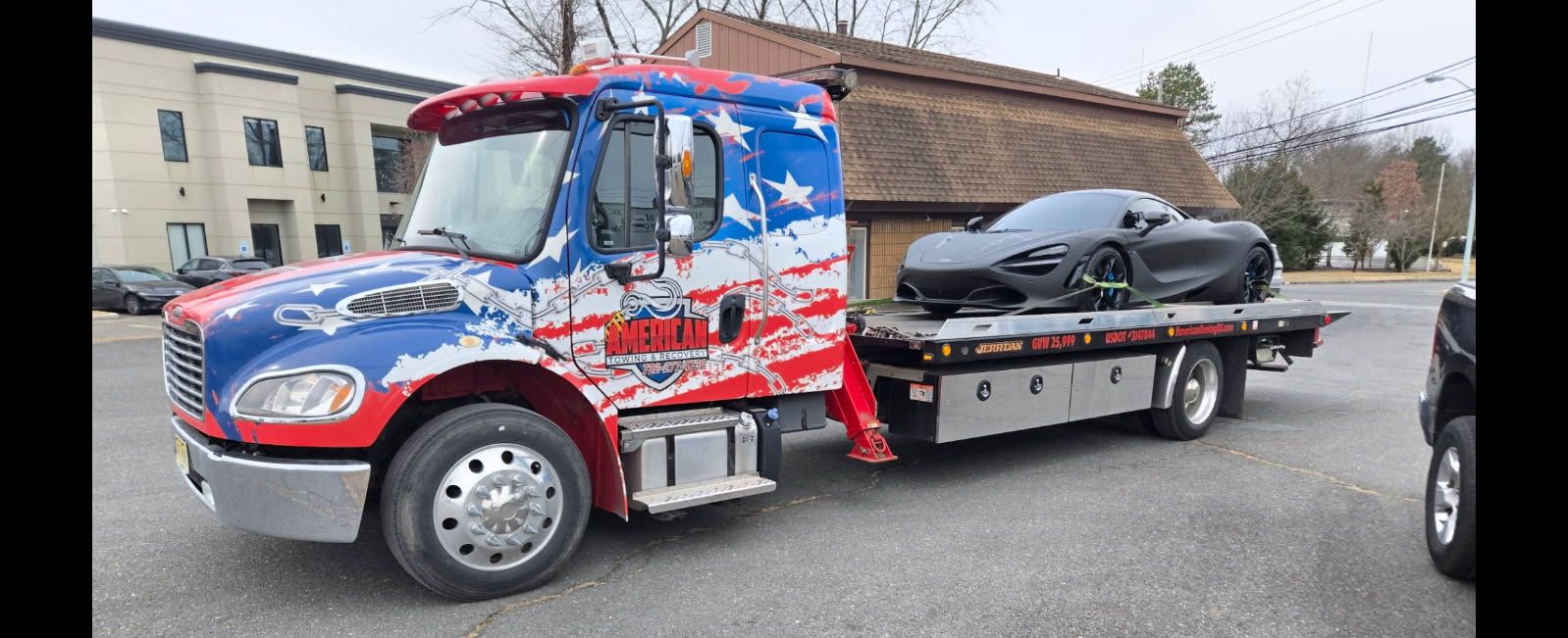 Tow truck with patriotic design carrying a black sports car.