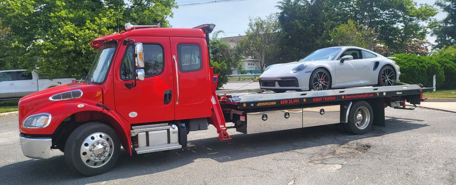 Red tow truck hauling a silver sports car on a sunny day.