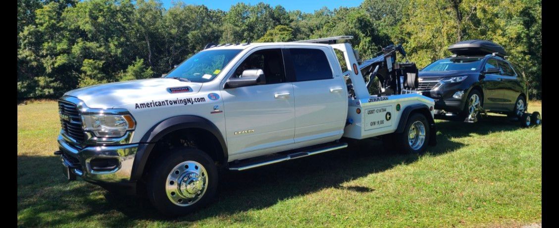 White tow truck towing a black SUV on a grassy area near trees under a blue sky.