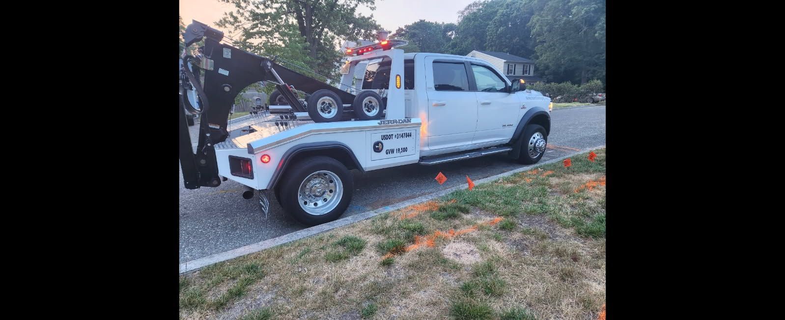 A white tow truck parked on a gravel driveway, with its tow arm extended.