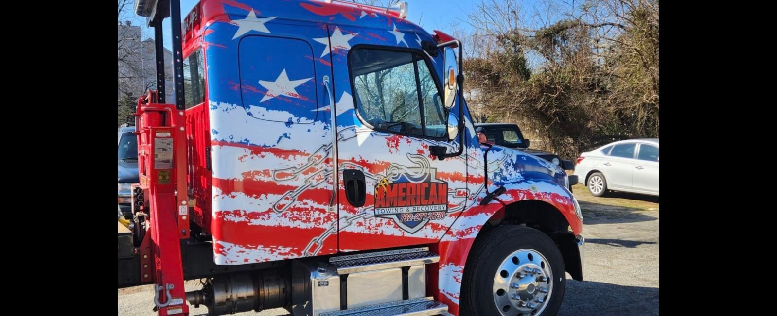 Tow truck with an American flag design. Red, white, and blue. Outdoors.