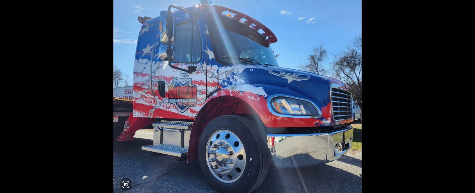 Semi-truck with American flag-themed paint job; red, white, and blue, parked outside on a sunny day.