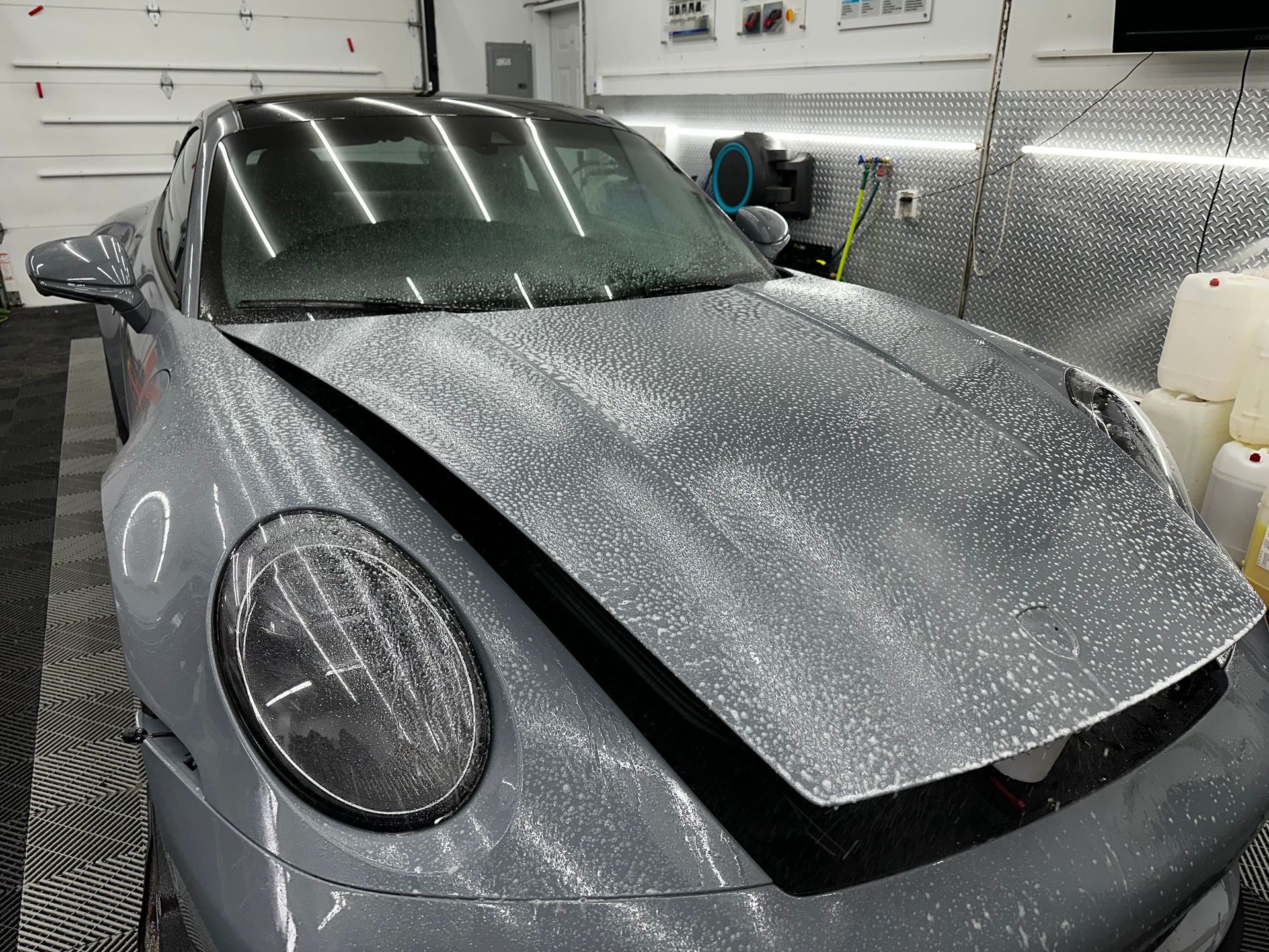 A silver car with a broken hood is sitting in a garage.