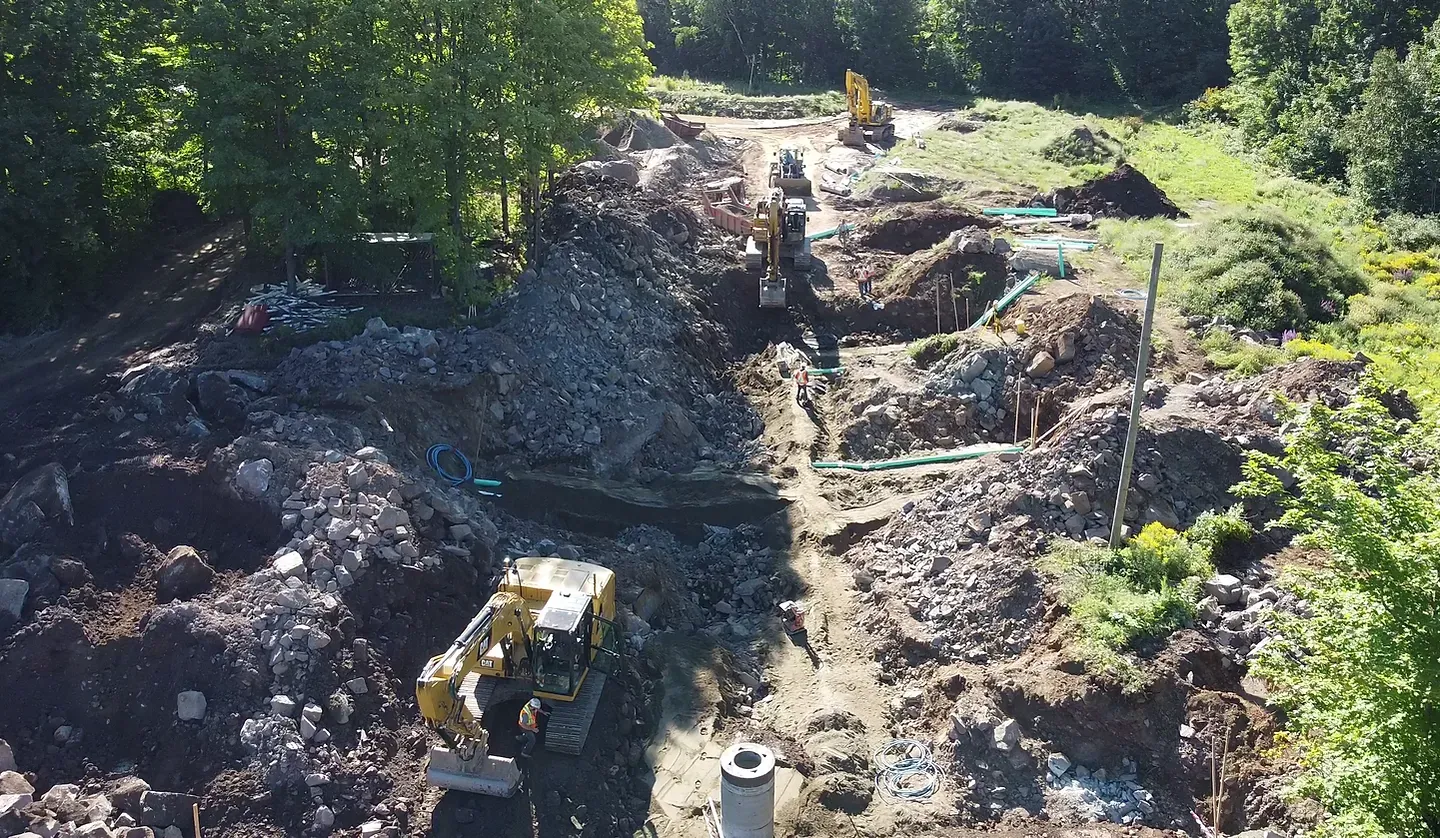 Vue aérienne d'engins de chantier creusant un terrain rocailleux entouré d'arbres par une journée ensoleillée.