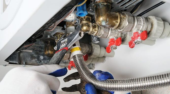 A person is fixing a water heater with a wrench and hose.