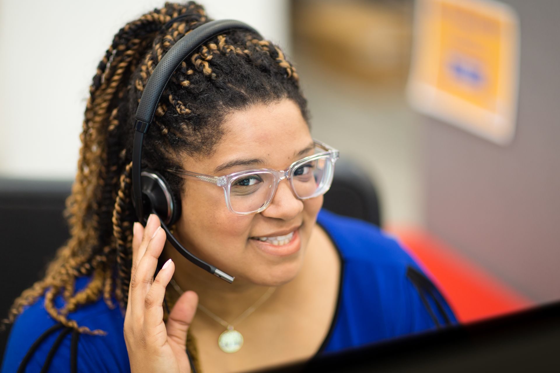 A woman wearing glasses and a headset is sitting in front of a computer.