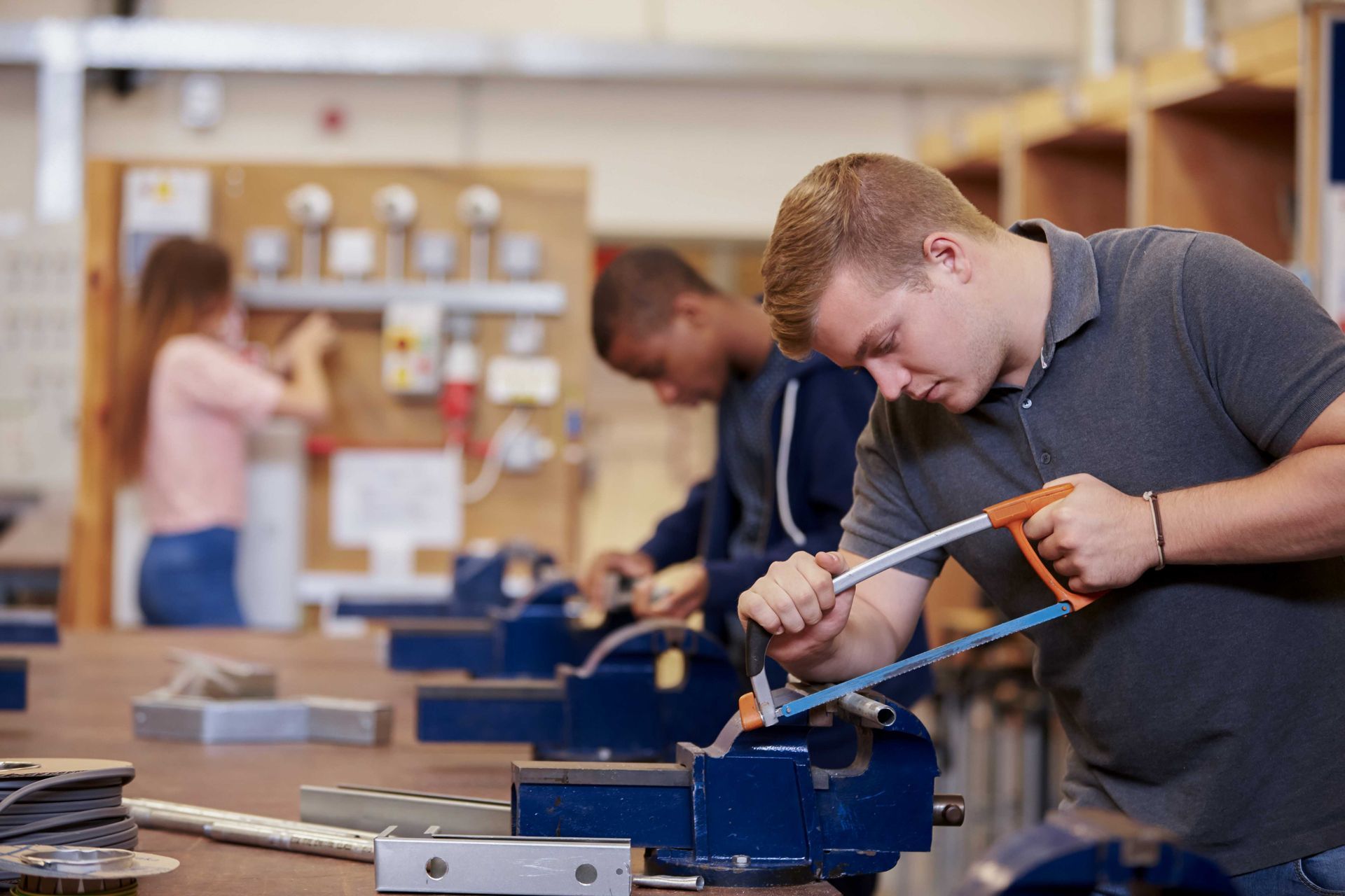 A man is cutting a piece of metal with a saw in a workshop.