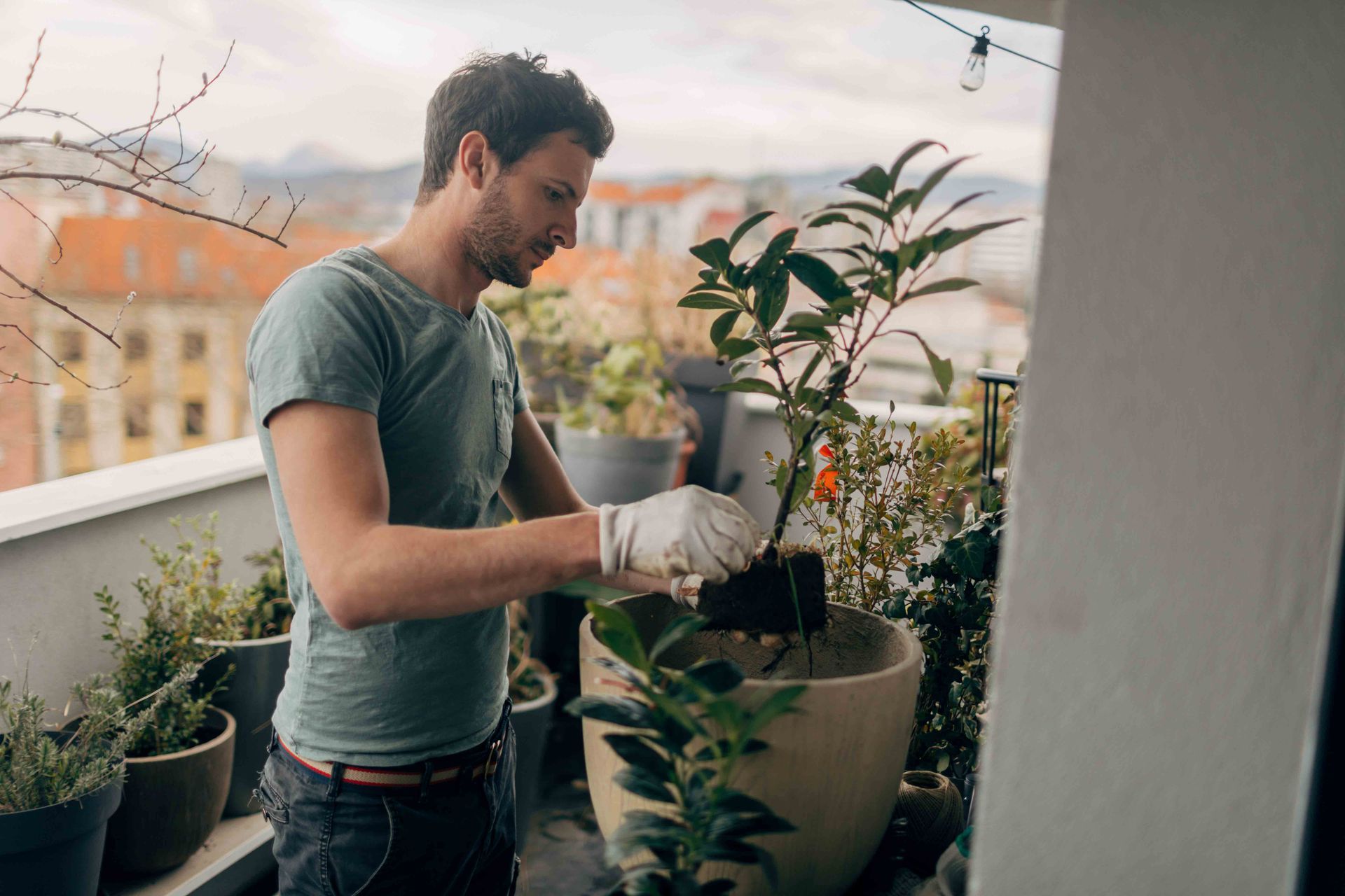 A man is planting a plant in a pot on a balcony.