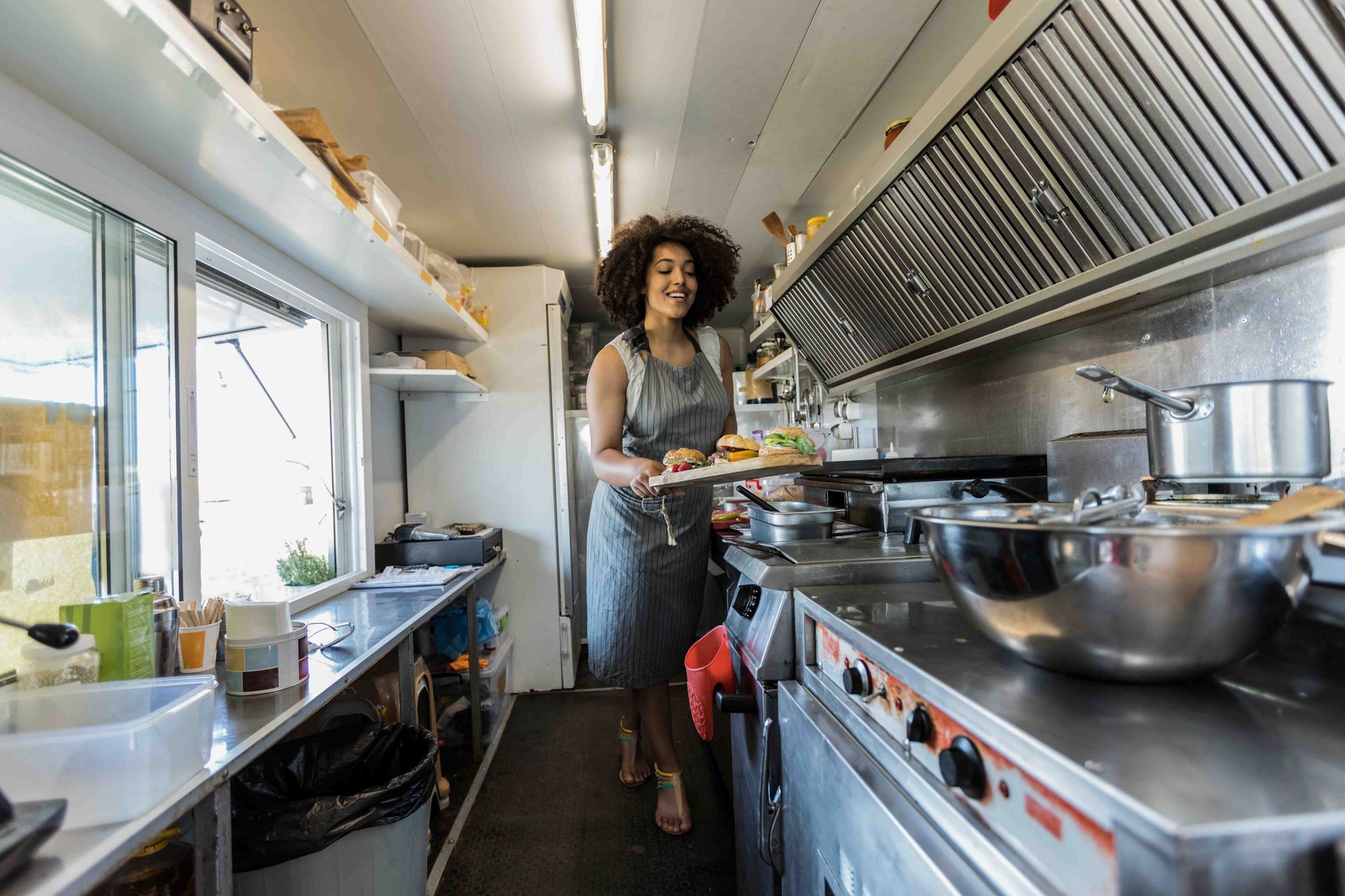 A woman is standing in a kitchen holding a tray of food.