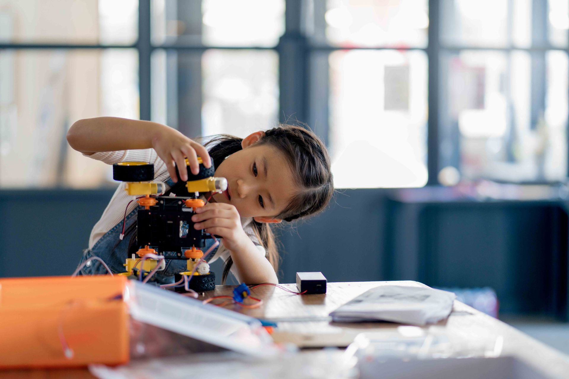 A little girl is sitting at a table working on a robot.
