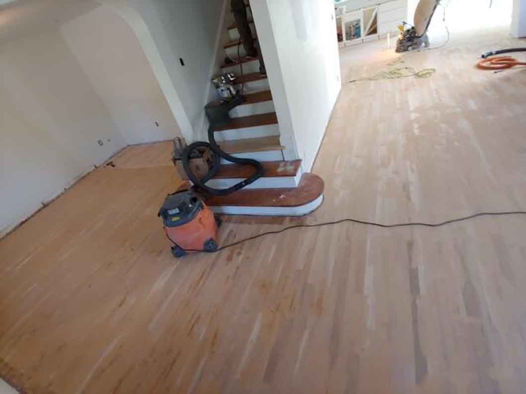 A vacuum cleaner is sitting on a wooden floor next to a set of stairs.