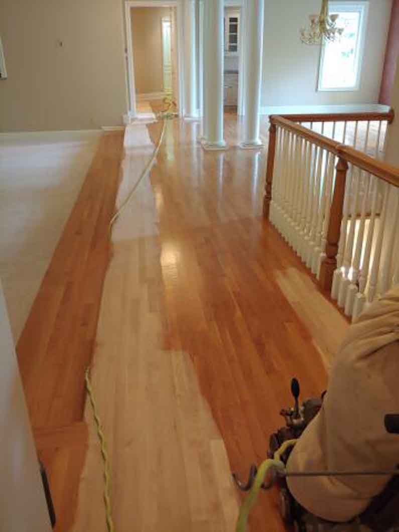 A person is painting a wooden floor in a hallway.
