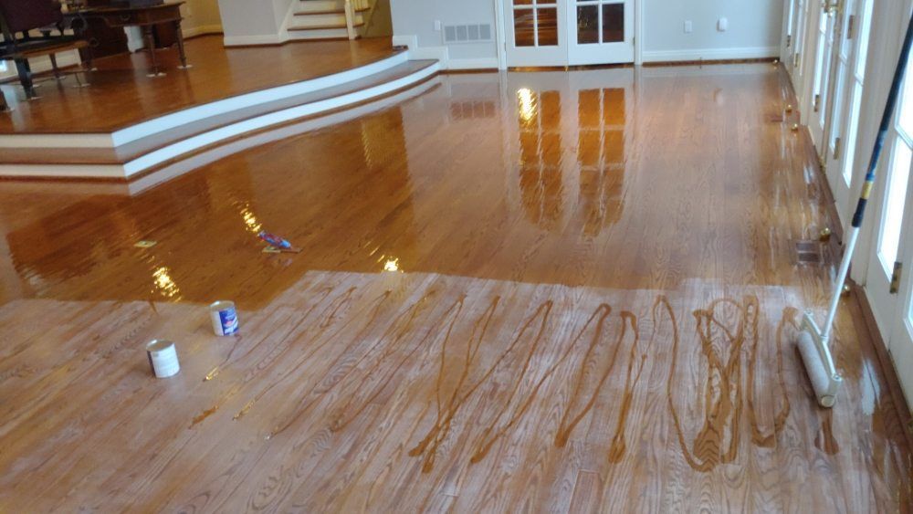 A person is painting a wooden floor in a living room.