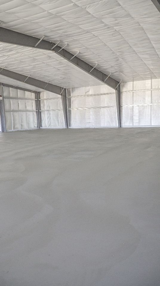 An unfinished, empty concrete room with structural pillars and window frames in a building under construction.