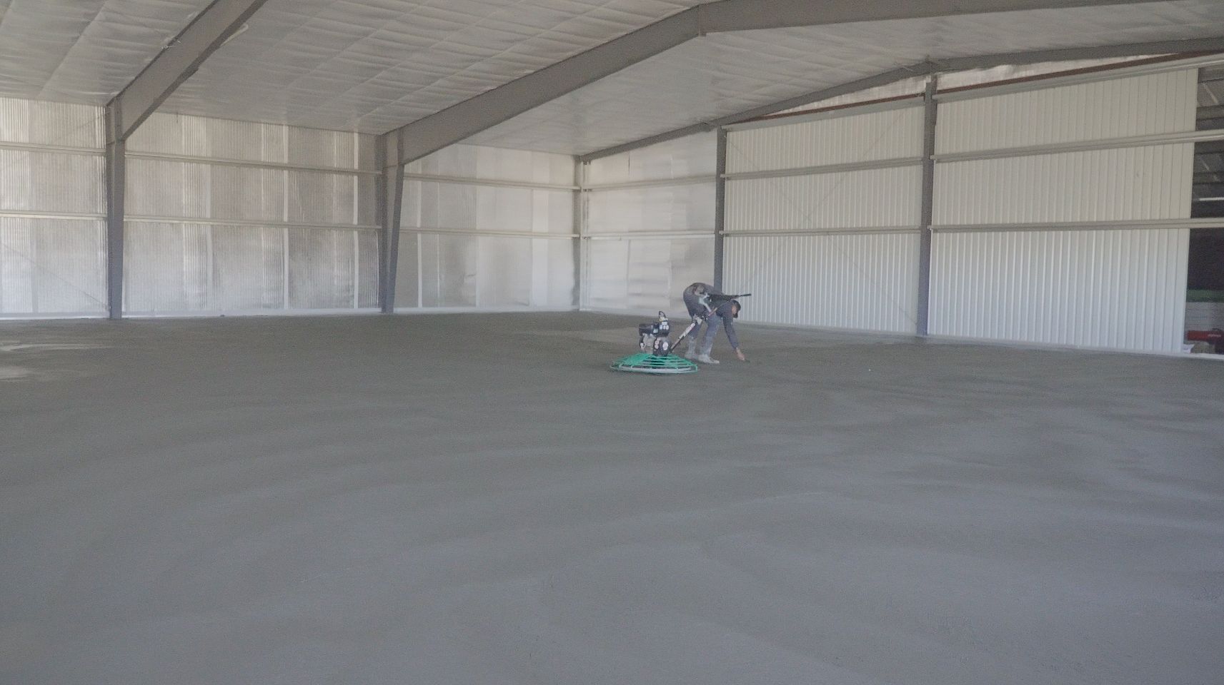 An unfinished, open-plan interior space with gray concrete walls, pillars, flooring, and large windows.