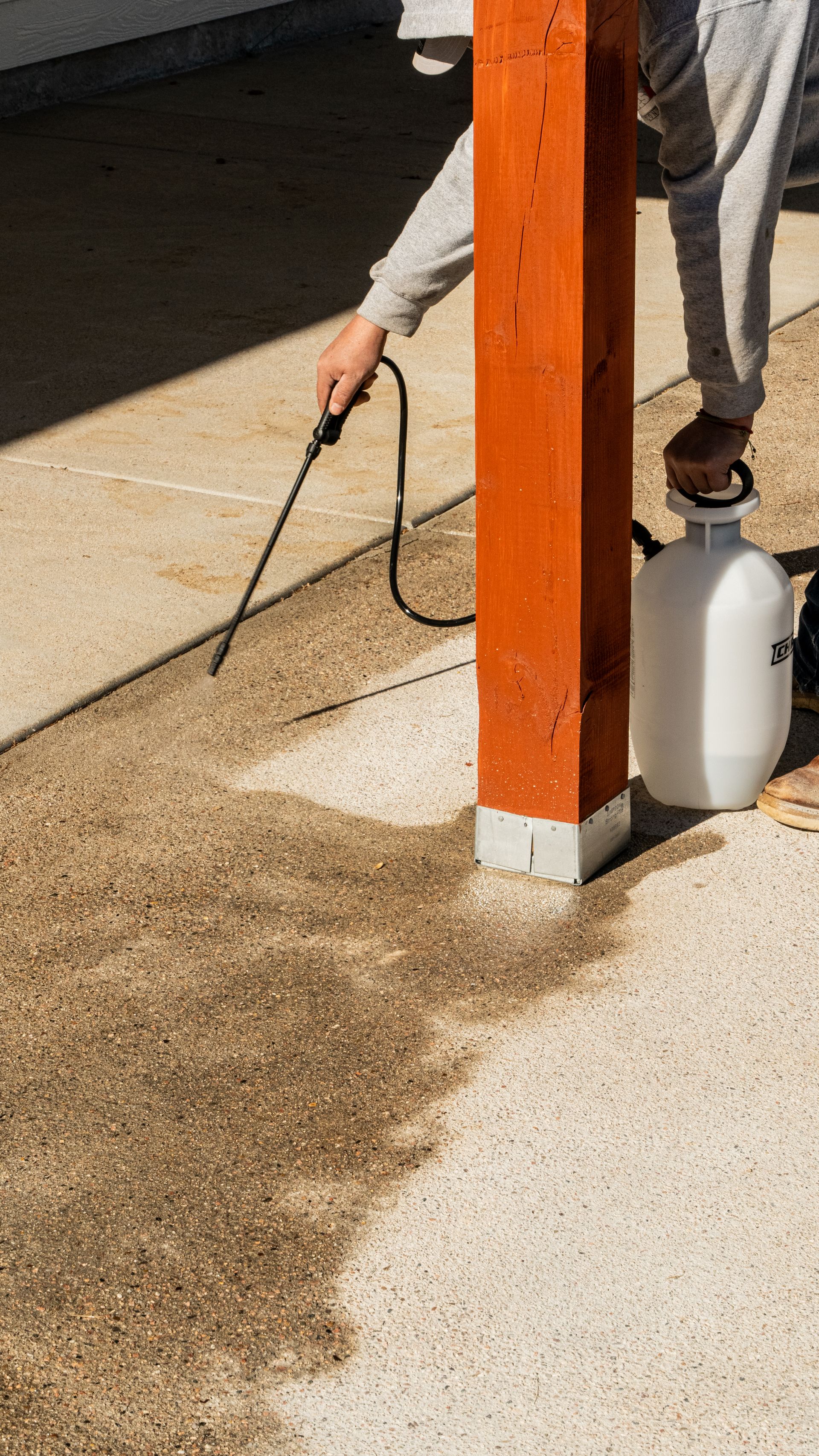 A gloved hand uses a metal trowel to smooth wet concrete inside a wooden formwork.