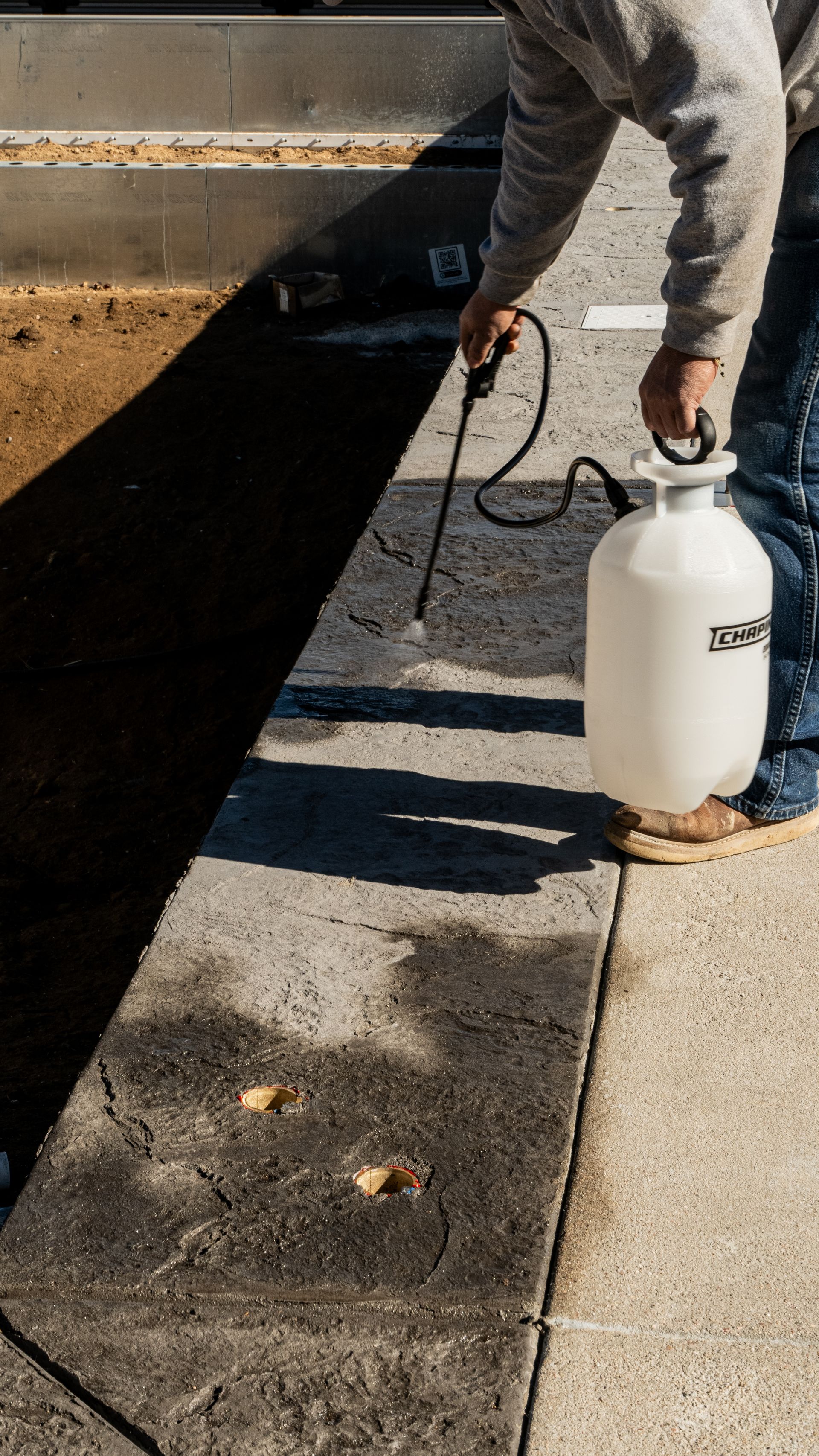 Workers in hard hats and safety gear pouring and leveling wet concrete onto a reinforced gravel surface at a construction site.