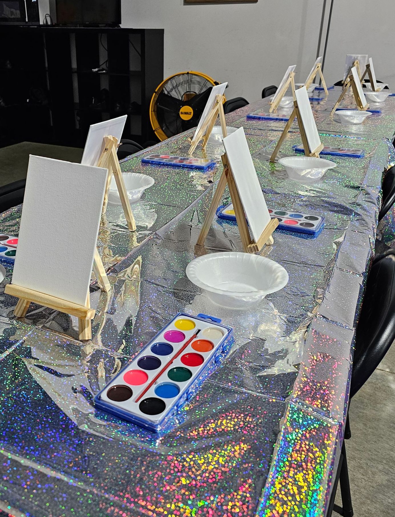 A long table with painting canvases and watercolors on it.