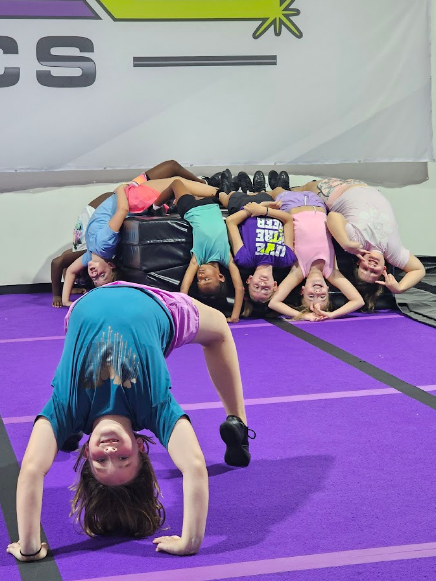 A group of children are doing handstands on a purple mat