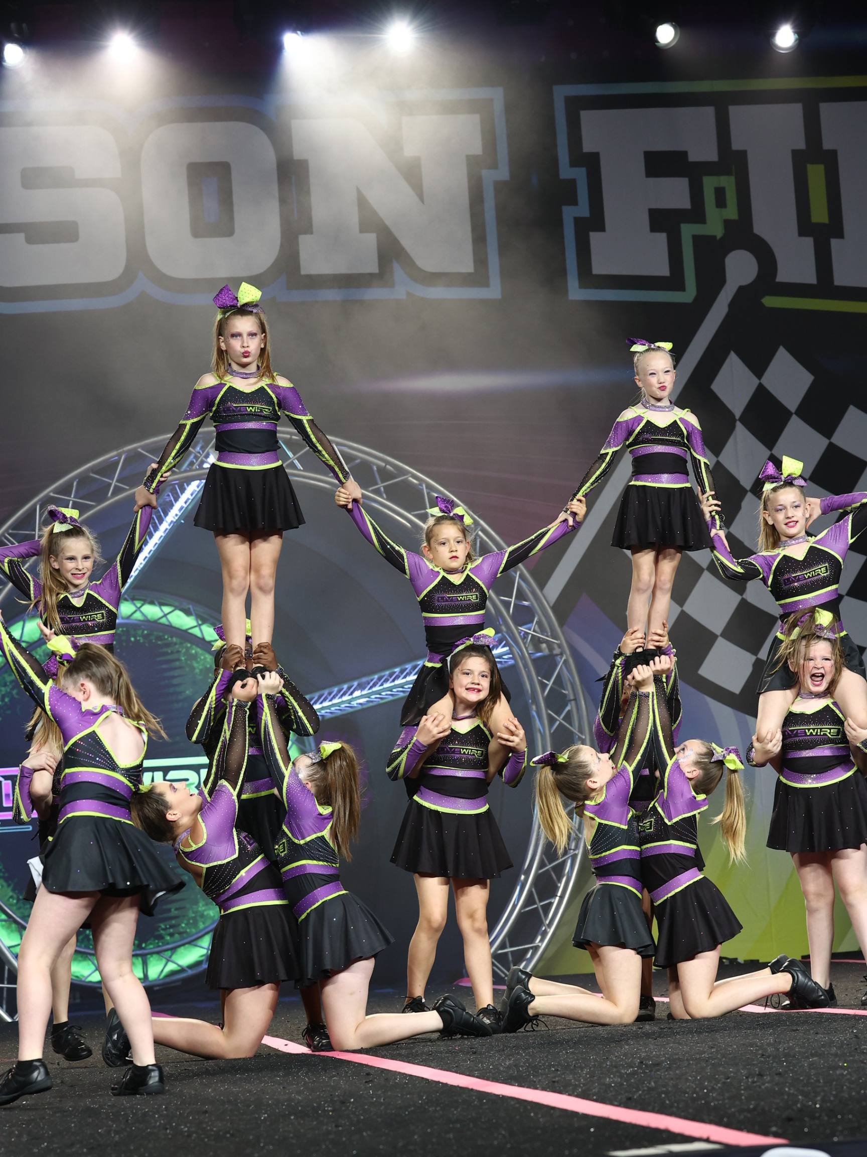 A group of cheerleaders are performing on a stage in front of a sign that says son fly