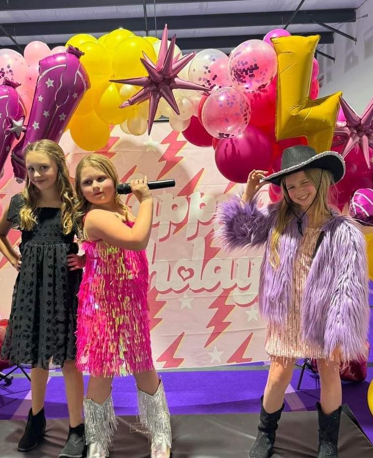 A group of young girls are standing next to each other in front of balloons.