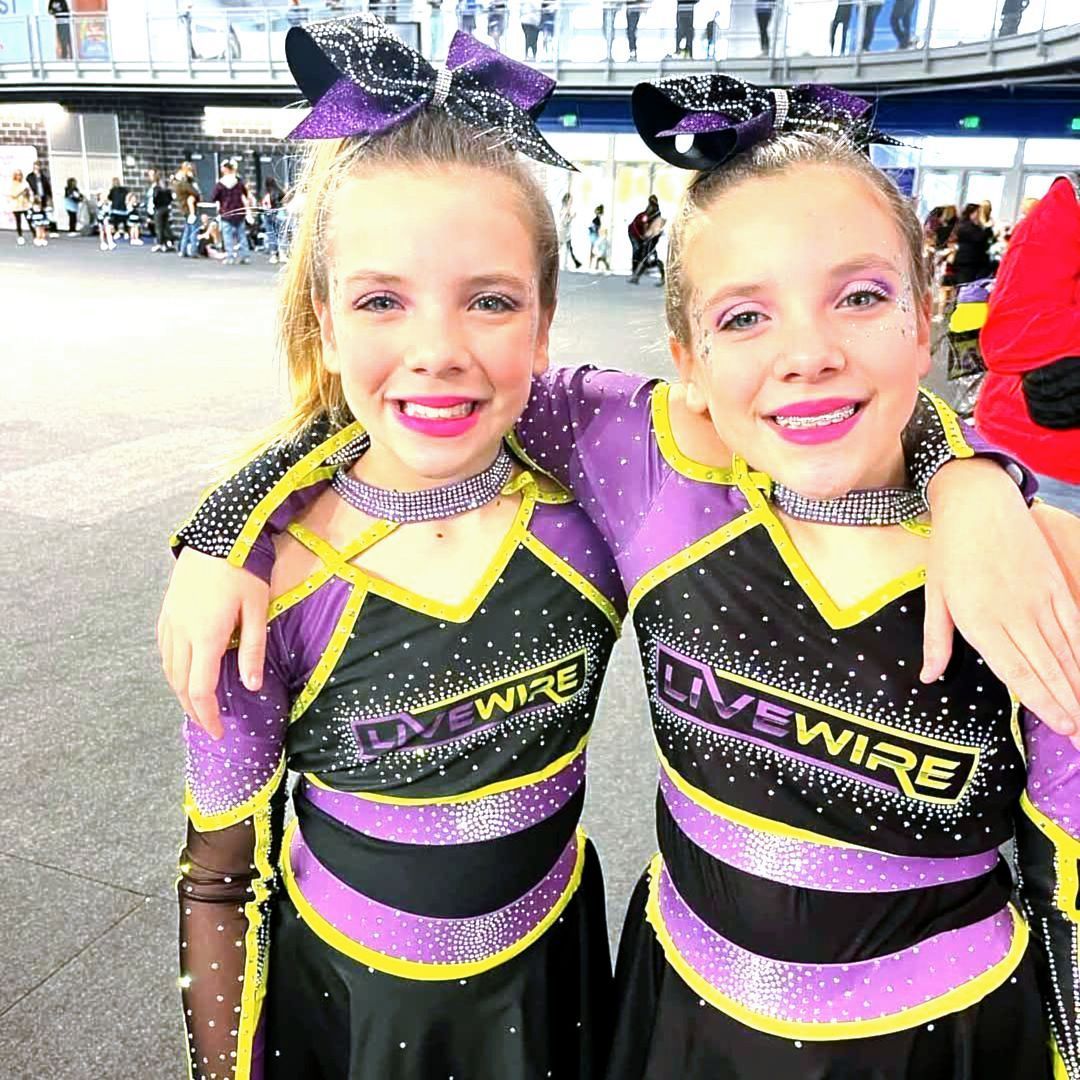 Two cheerleaders wearing purple and black uniforms are posing for a picture.