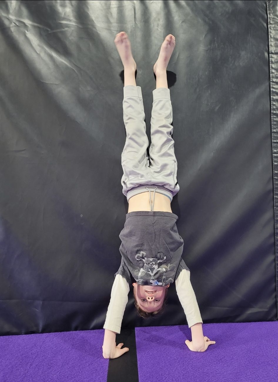 A young boy is doing a handstand on a trampoline.