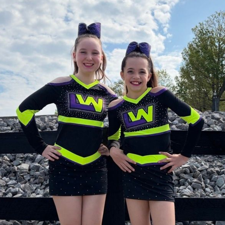 Two cheerleaders wearing purple and black uniforms are posing for a picture.