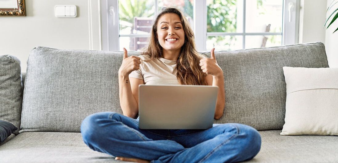 Woman sitting on couch with laptop giving two thumbs up