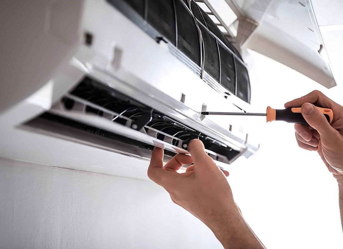 A person is fixing an air conditioner with a screwdriver.