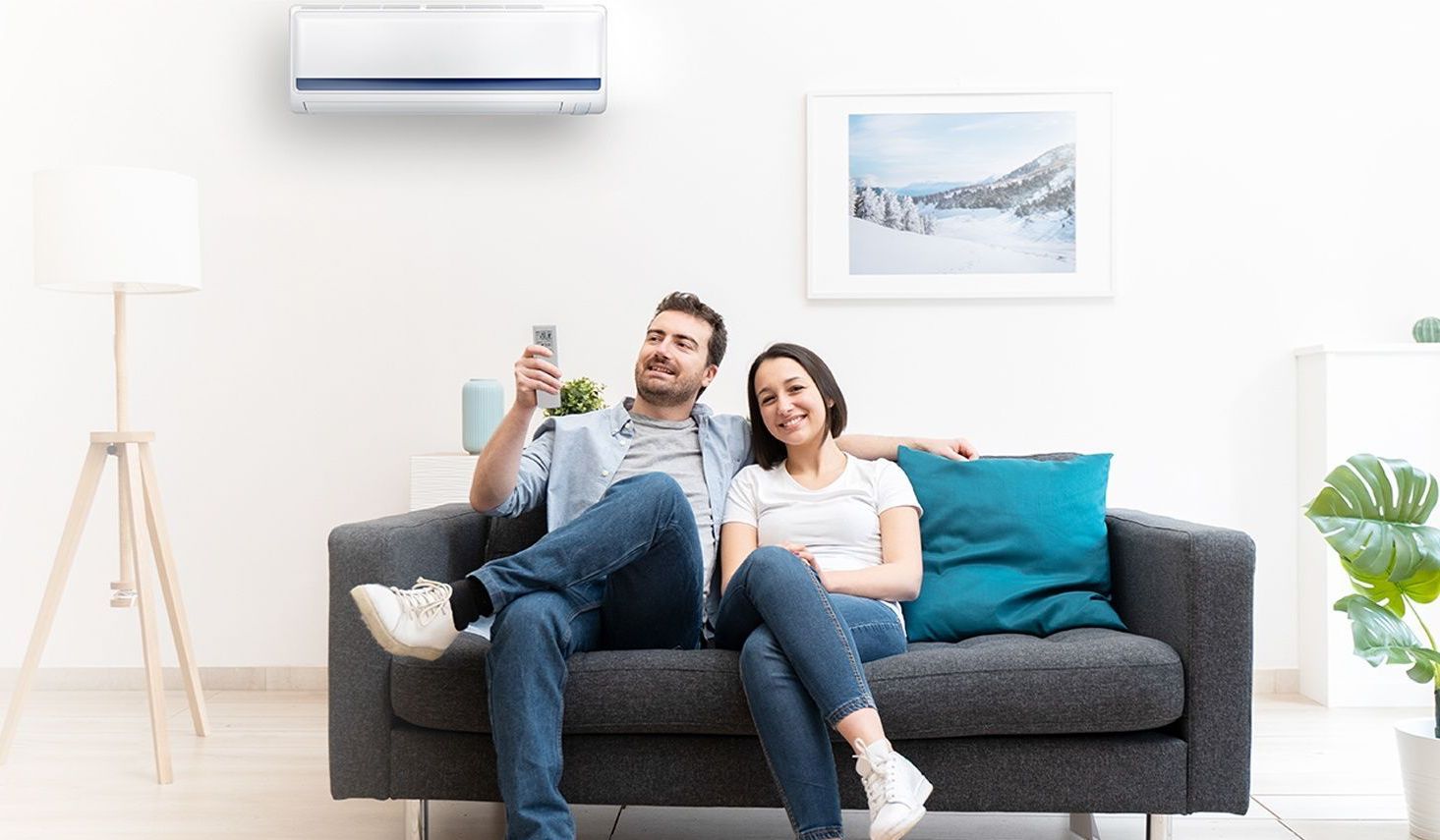 A man and a woman are sitting on a couch under an air conditioner.