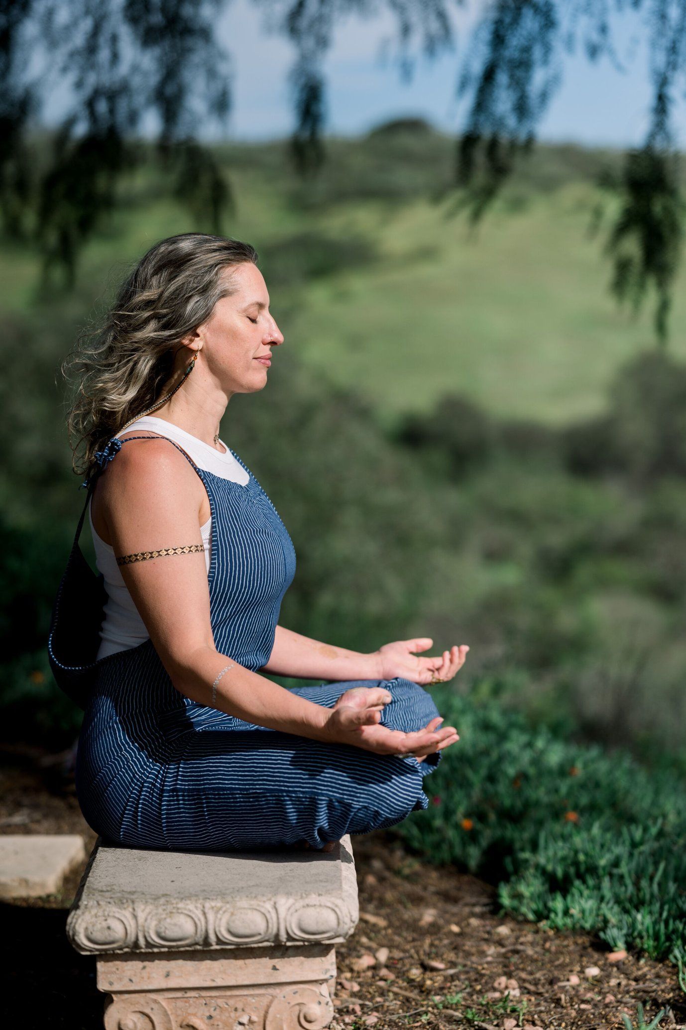 A woman is sitting on a stone bench in a lotus position with her eyes closed — Marie McAneney In Walkervale, QLD