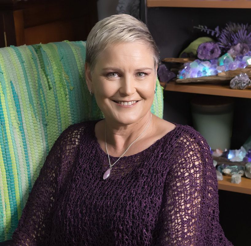 Woman Is Sitting In A Chair Wearing A Purple Sweater And A Necklace — Marie McAneney In Walkervale, QLD