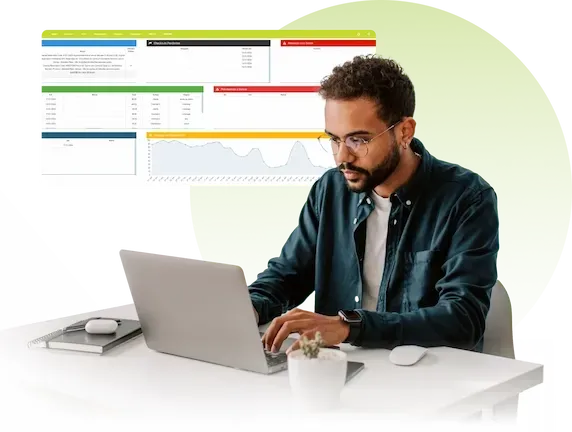 Homem digitando em um laptop em uma mesa branca com gráficos analíticos coloridos exibidos atrás dele.