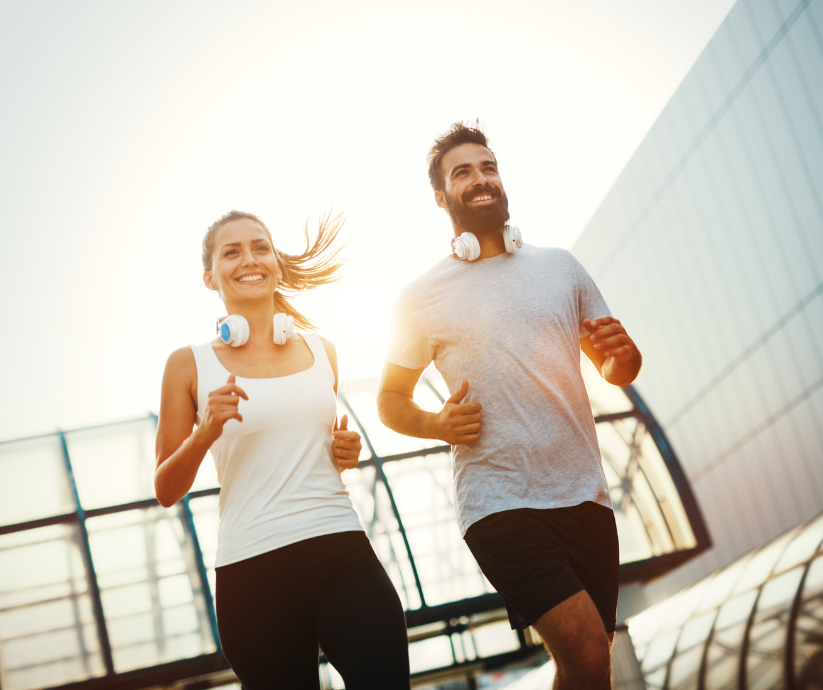 Woman and man running outdoors, both smiling, with headphones on, near a modern building.
