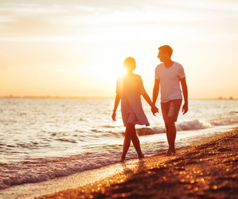 Couple holding hands walking on a beach at sunset.