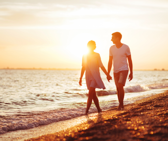 Couple holding hands walking on a beach at sunset.