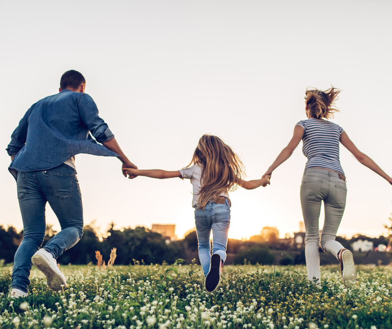 Family running through a grassy field at sunset, holding hands.