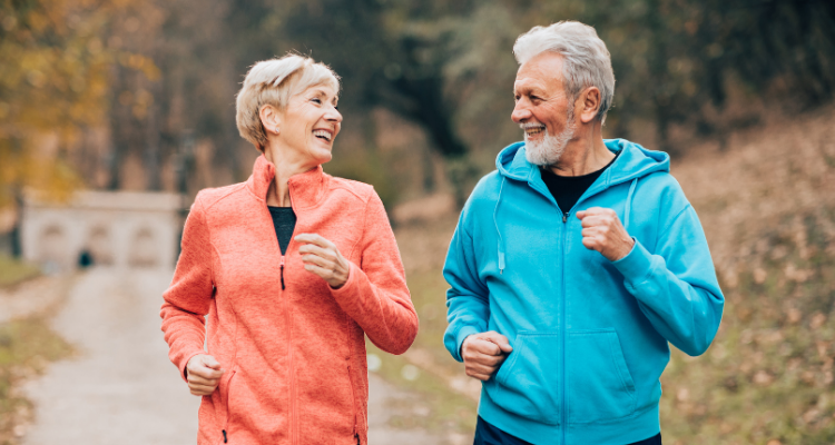 Couple jogging on a path, smiling. Woman in orange, man in blue, outdoors in autumn.