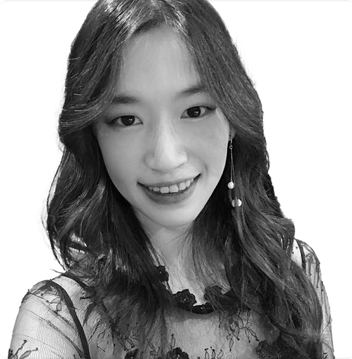 Woman with freckles smiles, wearing a black lace top and earring, in a round, outdoor portrait.