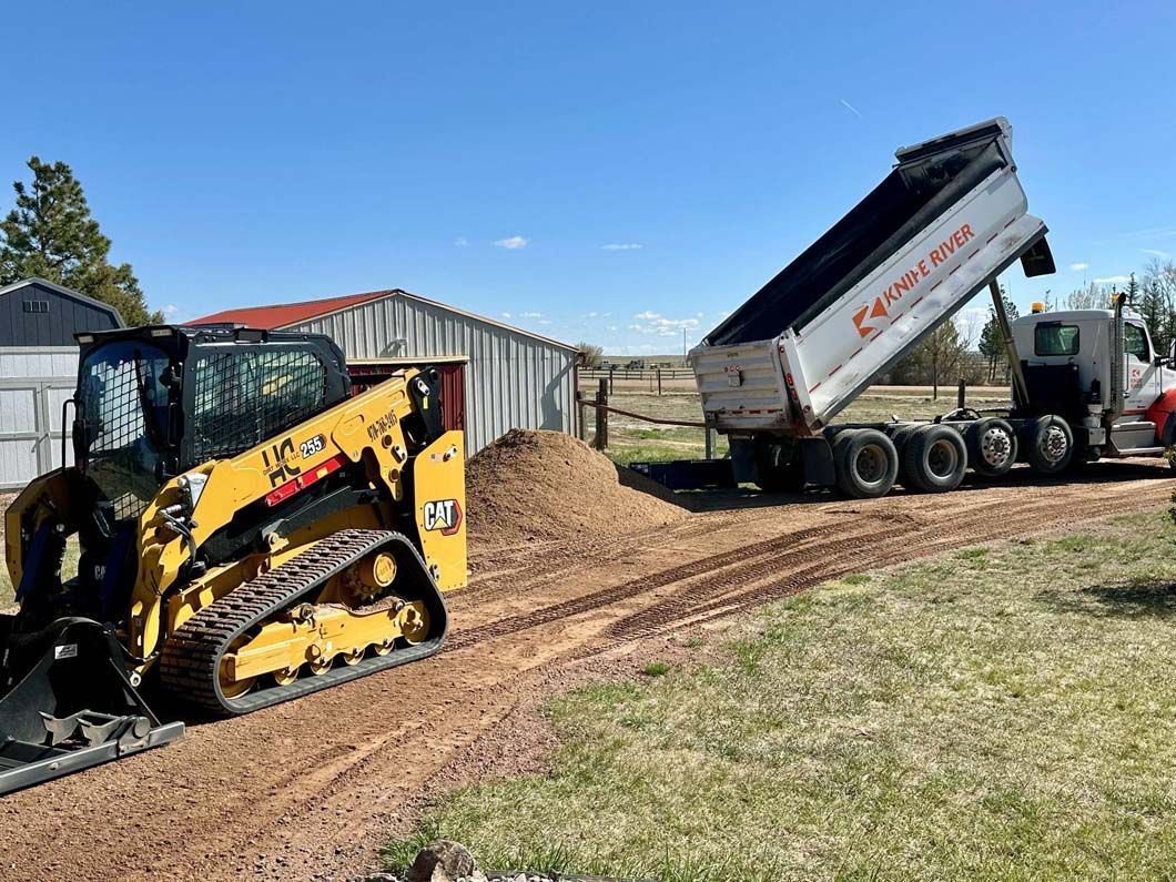 A bulldozer is loading a dump truck with dirt on a dirt road.