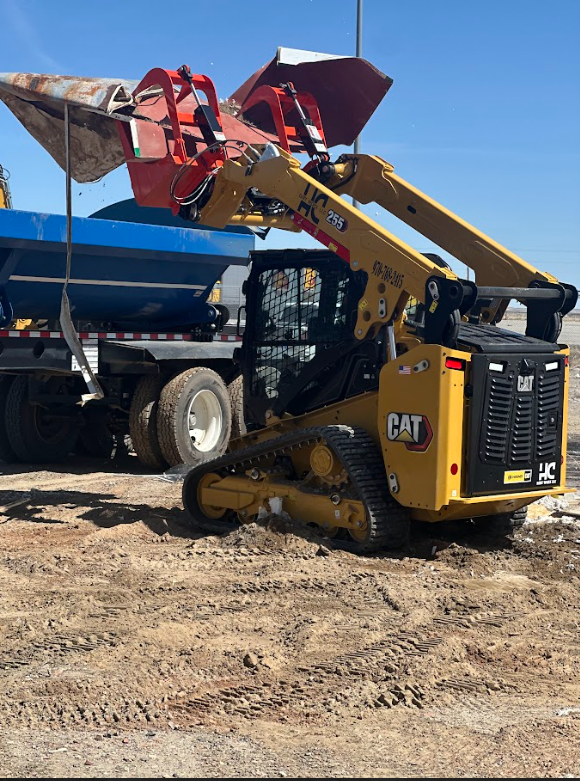 A cat skid steer is loading dirt into a dump truck.