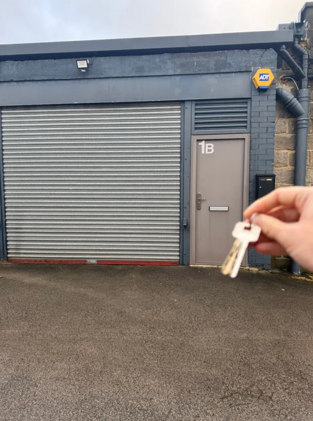 A person is holding a pair of keys in front of a garage door with the number 1b on it