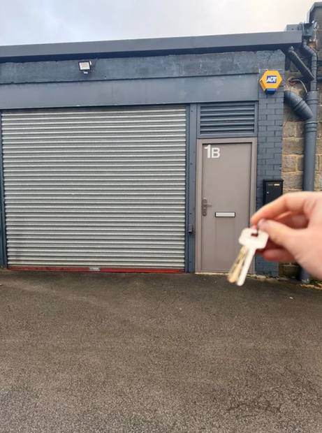 A person is holding a pair of keys in front of a garage door with the number 1b on it