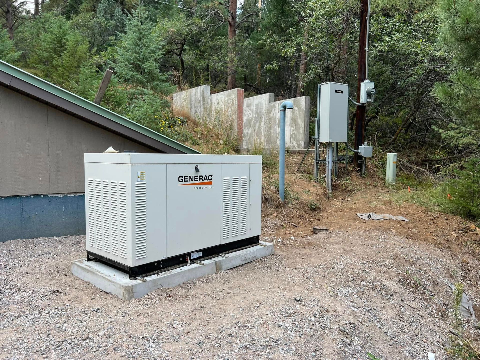A generator next to a house with electrical equipment, set in a wooded area.