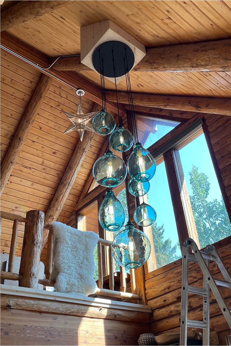 Chandelier with blue glass bulbs hangs from wood ceiling in a rustic interior.