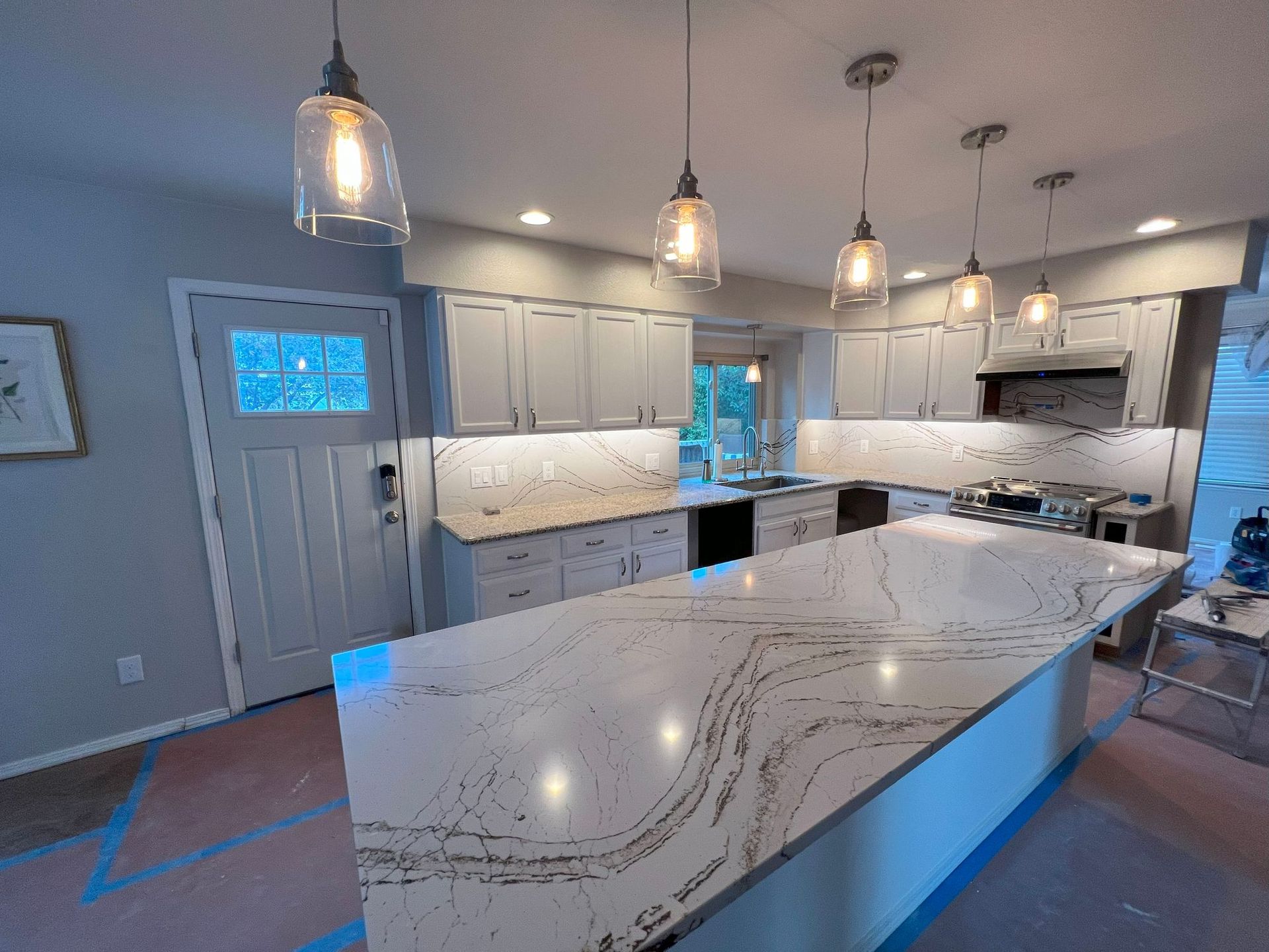 Newly renovated kitchen with a large island and pendant lights. White cabinets and countertops.