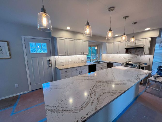 Newly renovated kitchen with a large island and pendant lights. White cabinets and countertops.
